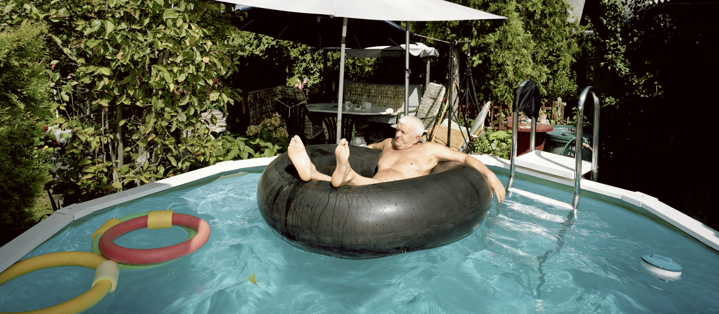 Ein alter Mann sitzt in einem Schwimmring in einem Gartenpool.