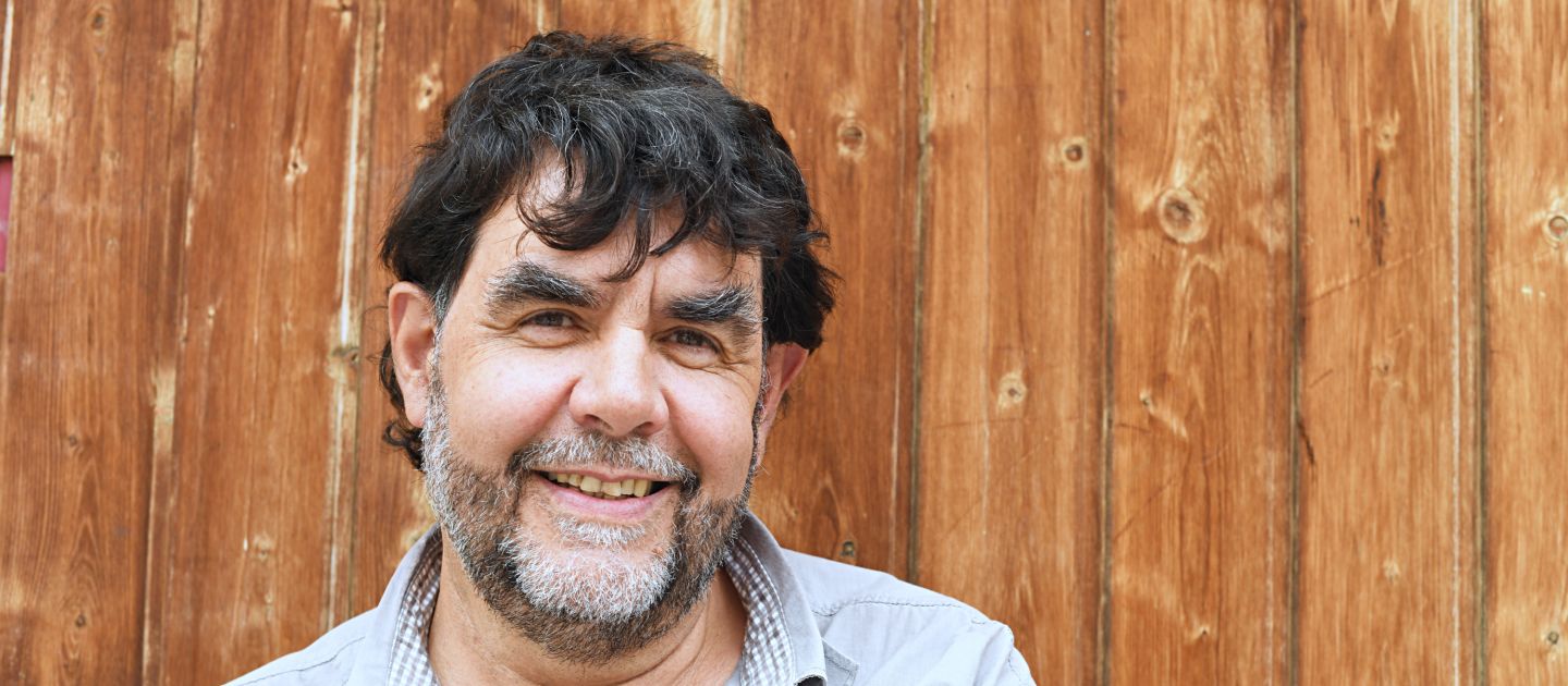 Hubert Schmid Ein Porträtfoto von Hubert Schmid vor einem hölzernen Hintergrund.