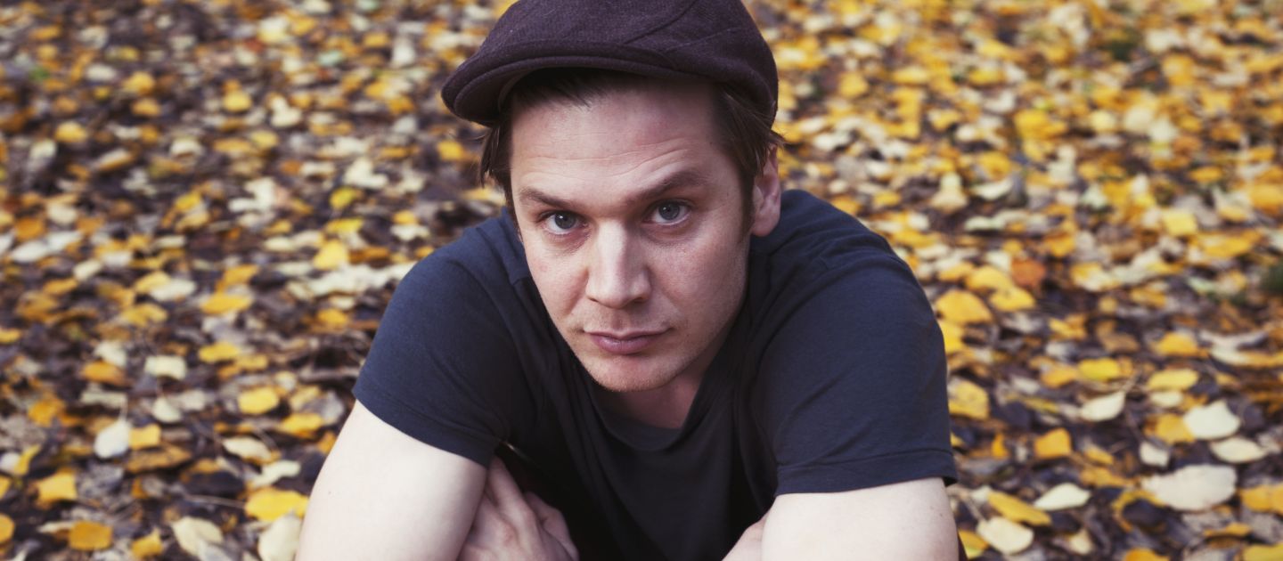 Das Foto zeigt ein Porträt von Justin Mühlenhardt zwischen Herbstblättern. Er trägt eine Kappe.
