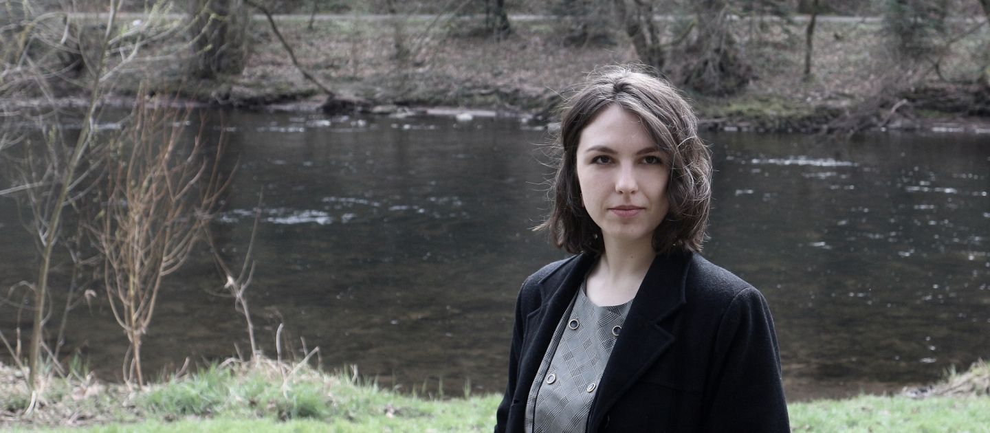 Das Foto zeigt Sonja Hoyler in einem Wald vor einem Fluss