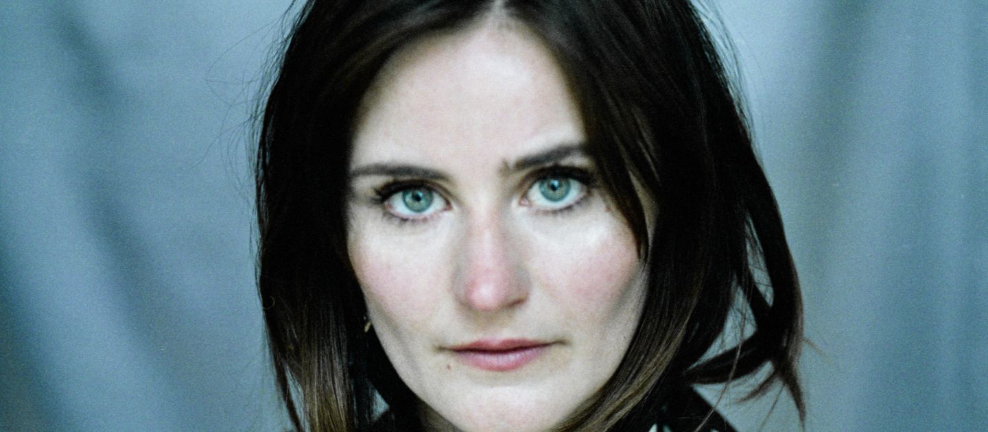 Ein Portraitfoto von Eleonore Carrière vor blauem Hintergrund mit einem gepunkteten Halztuch.