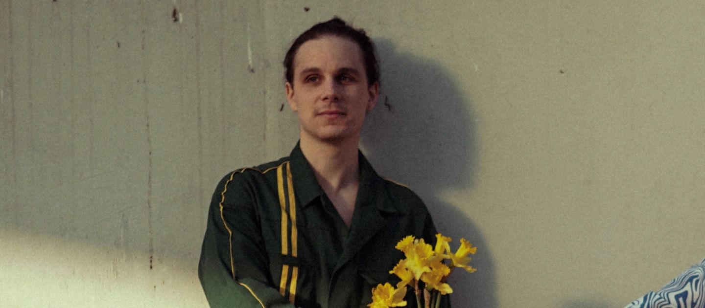 Alexander Zwick steht vor einer Wand und ihm wird ein gelber Blumenstrauß in die Hand gereicht.