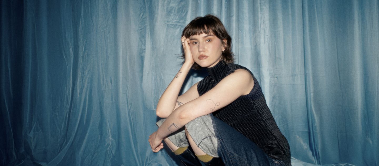 Maja Beyer (c) Marf Mabo Maja Beyer sitzt in der Hock vor einem blauen Vorhang.