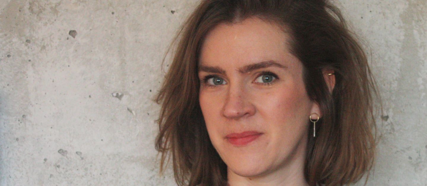 Nadin Schumacher steht vor einer Wand und trägt ein  schwarzes T-Shirt.