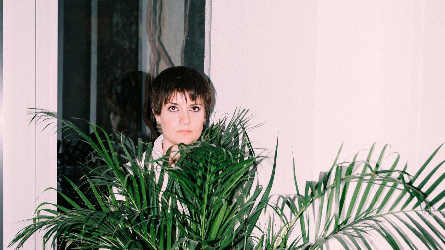 Christina Tscharyiski im weißen Einteiler hinter einer Palme.