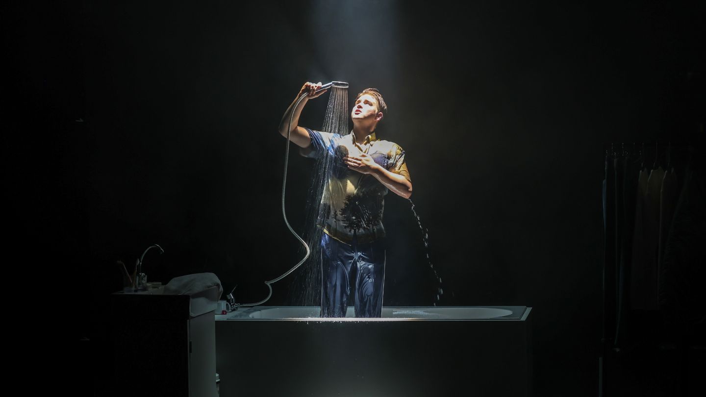 Arbeit und Struktur: Moritz Klaus (c) Melanie Zanin Ein Produktionsfoto von "Arbeit und Struktur". Moritz Klaus steht in einer Badewanne und duscht in seinen Klamotten.