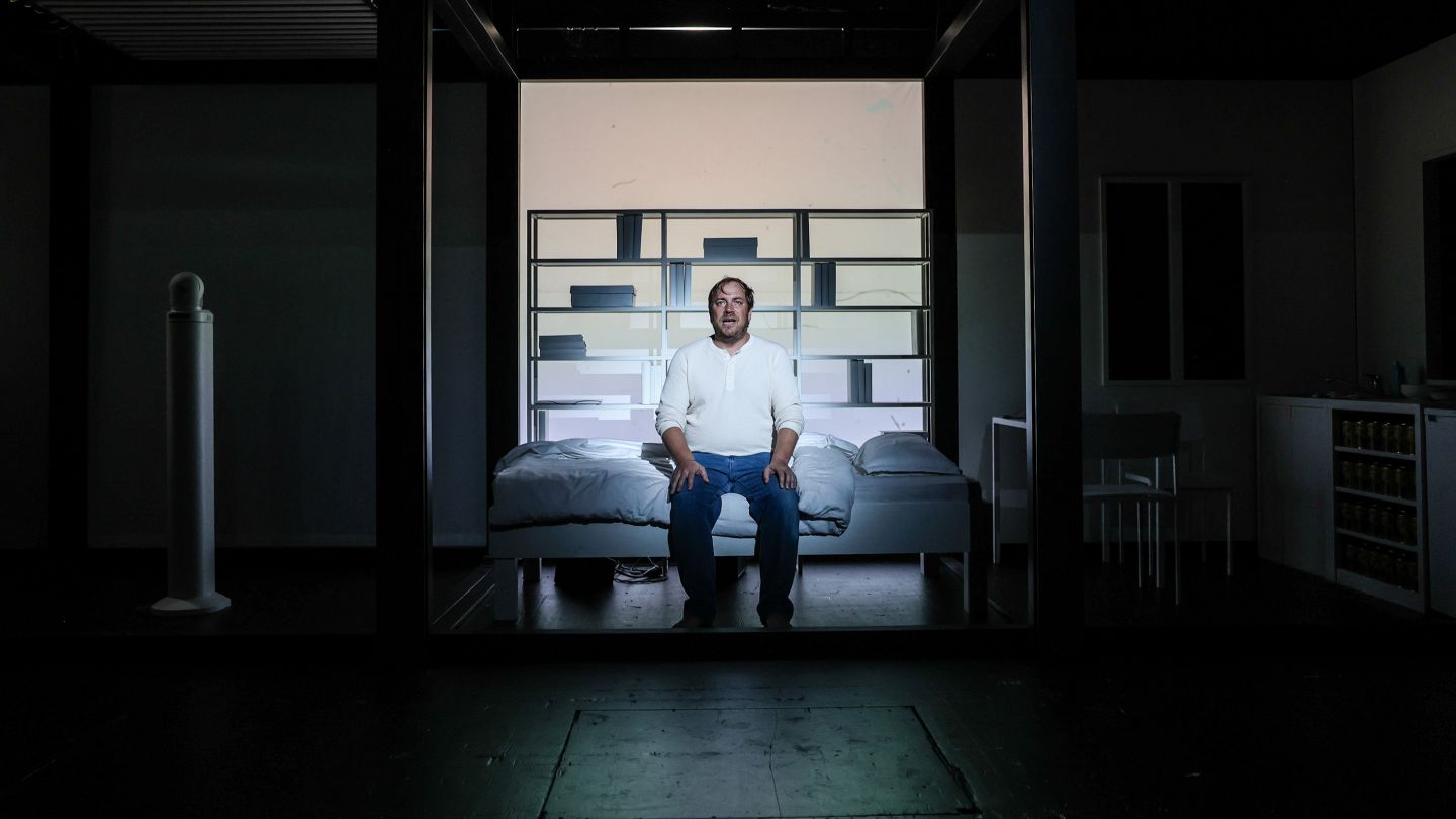 Florian Lange sitzt auf einem Bett im Scheinwerferlicht.