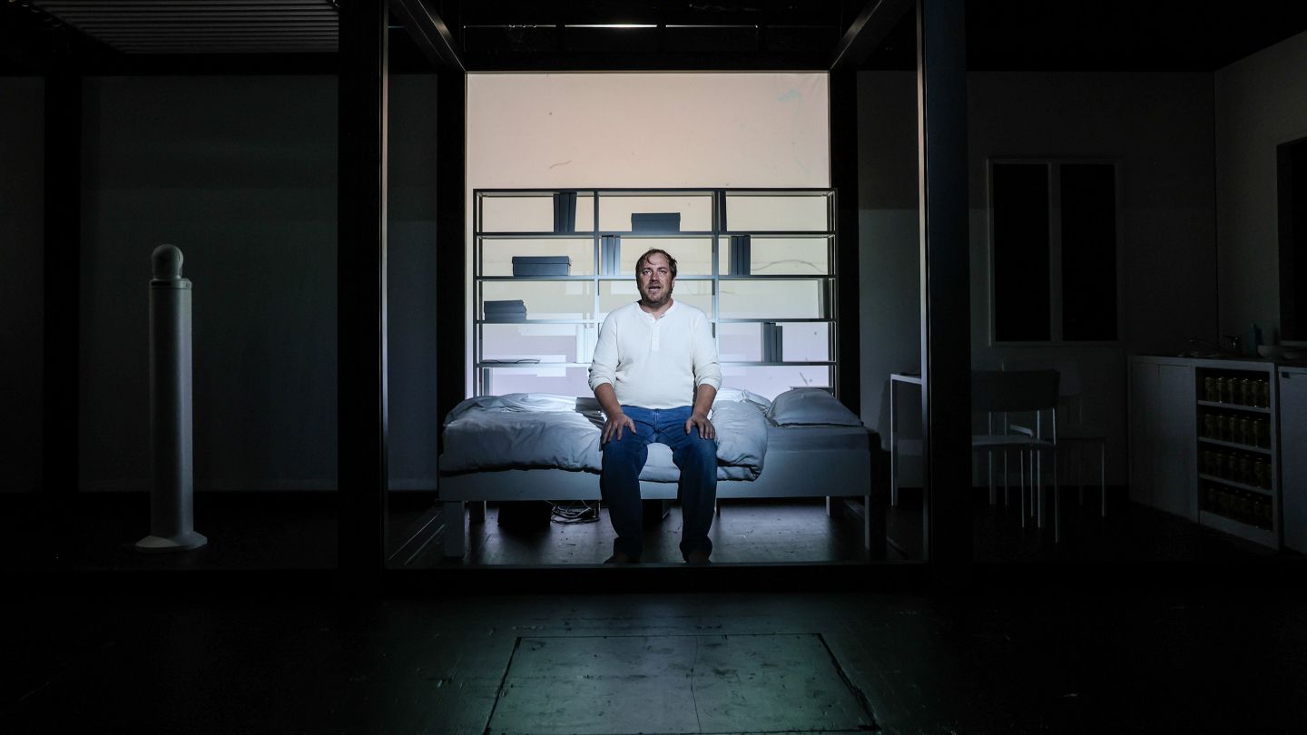 Arbeit und Struktur (c) Melanie Zanin Florian Lange sitzt auf einem Bett im Scheinwerferlicht.