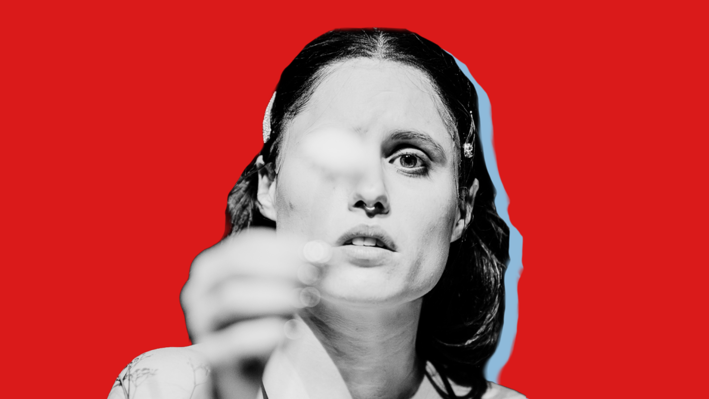 Eine Frau hält mit ernstem Gesicht eine Blume in die Kamera.