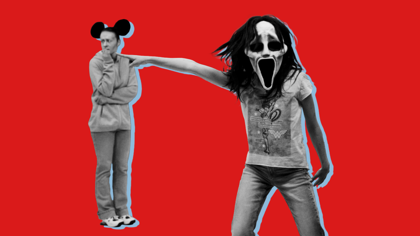 Eine Person mit gruseliger Maske zeigt mit ihrem Finger auf eine Person, die Mickey Mouse Ohren trägt.