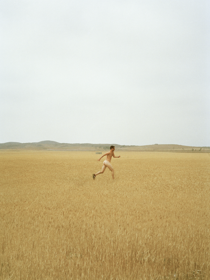 Das Foto zeigt einen nackten, laufenden Menschen auf einem Feld