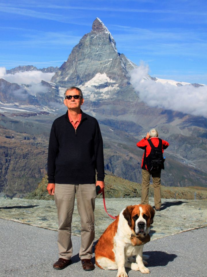 Das Foto zeigt einen Mann mit Hund vor Bergpanorama