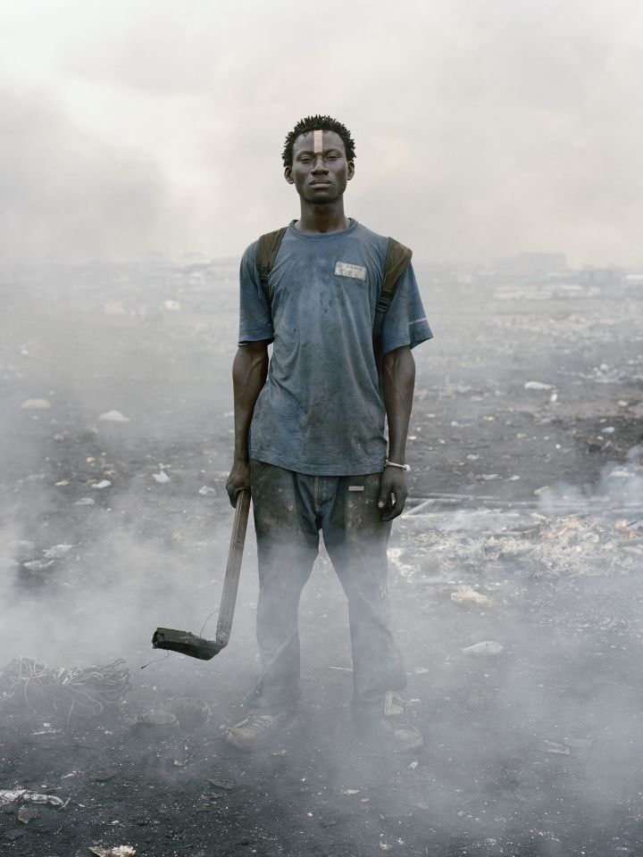 Ein junger Schwarzer Mann steht mit einer Hacke in der Hand inmitten von Schutt und Rauchwolken