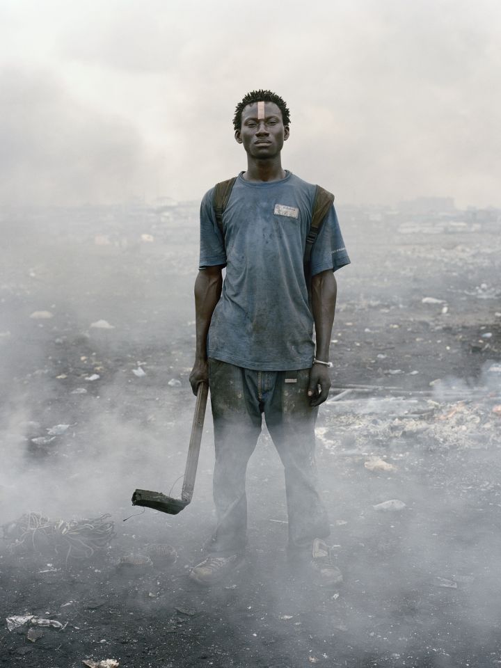 Ein junger Schwarzer Mann steht mit einer Hacke in der Hand inmitten von Schutt und Rauchwolken