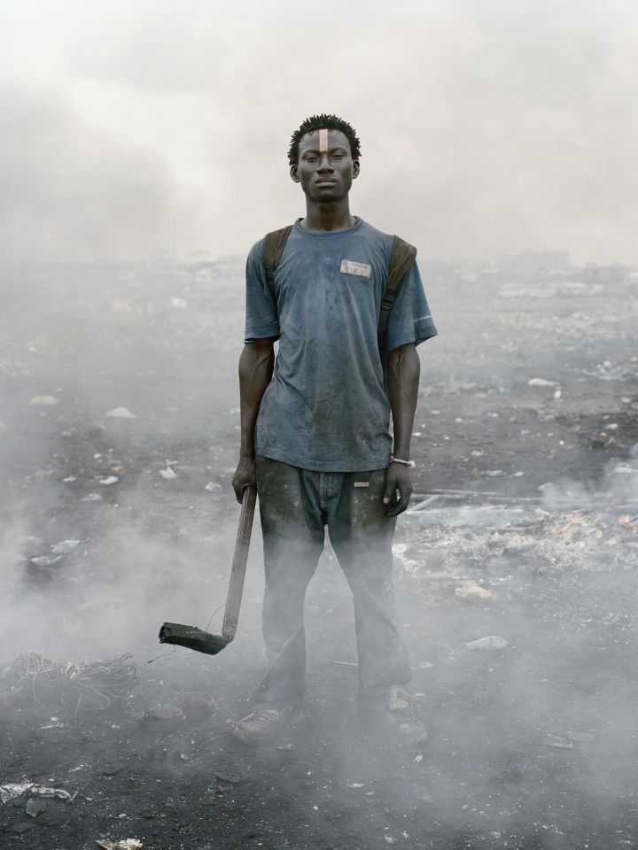 Ein junger Schwarzer Mann steht mit einer Hacke in der Hand inmitten von Schutt und Rauchwolken