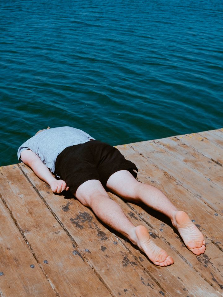 Das Plakatmotiv zeigt zeigt eine Person, die mit dem Bauch auf einem Steg liegt. Von den Schultern ab hängt der Körper über den Rand des Stegs hinaus, der Kopf ist nicht zu sehen.
