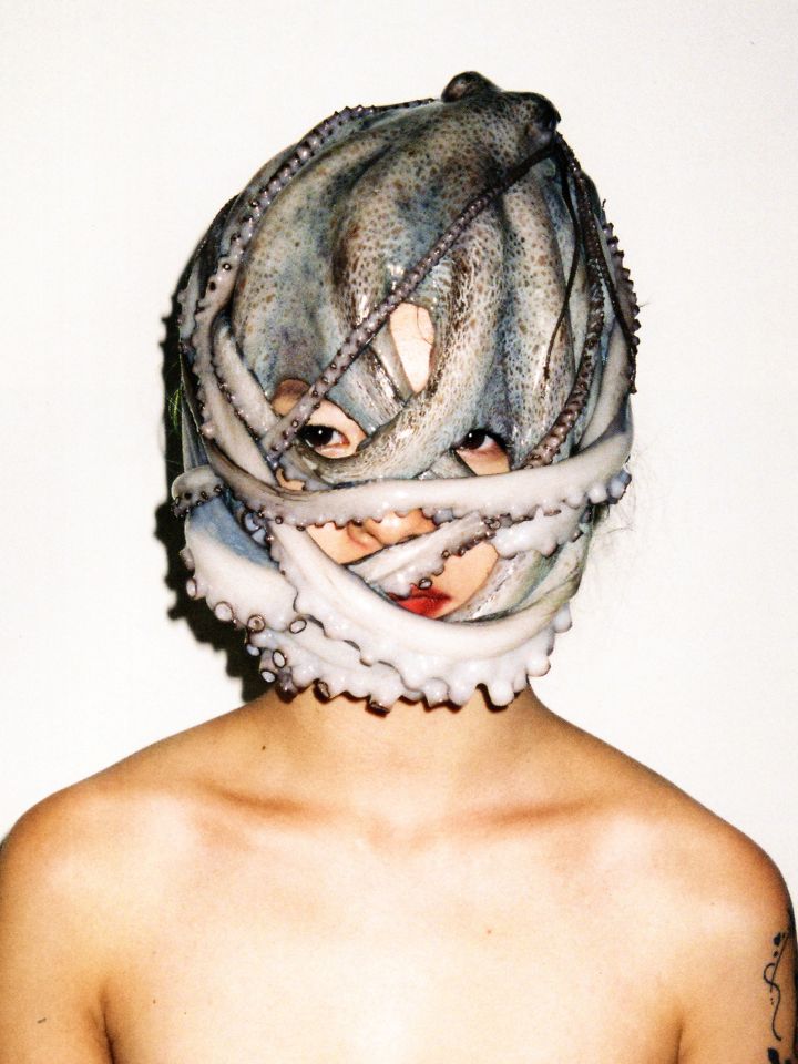 Eine Person vor weißem Hintergrund. Um ihren Kopf ist ein Oktopus gewickelt.