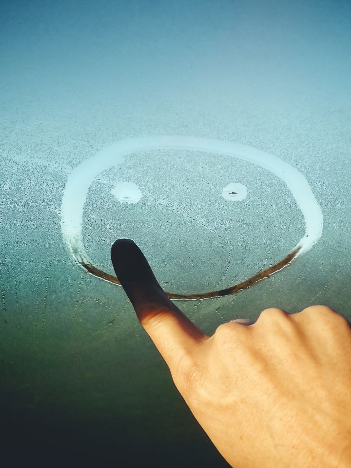 Eine Hand malt einen Smiley auf ein beschlagenes Glas.