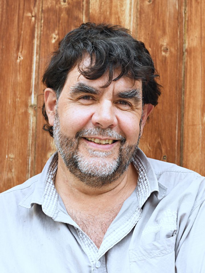 Ein Porträtfoto von Hubert Schmid vor einem hölzernen Hintergrund.