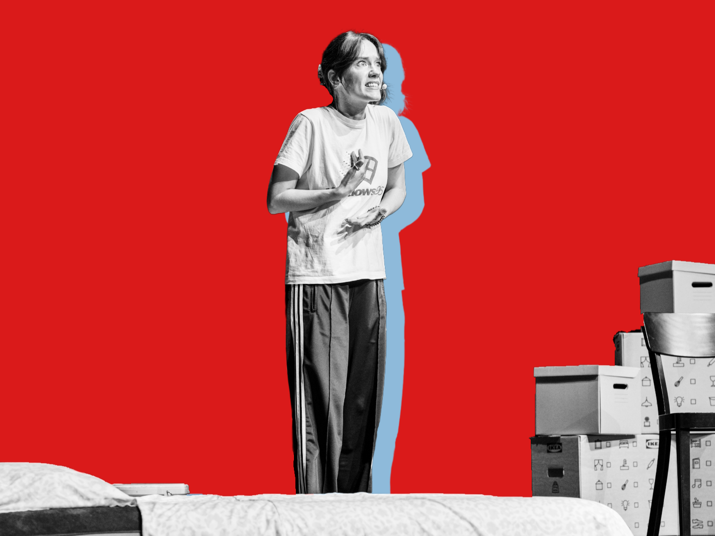 Eine Frau steht auf der Bühne, hinter ihr Umzugsboxen und ein Stuhl. 