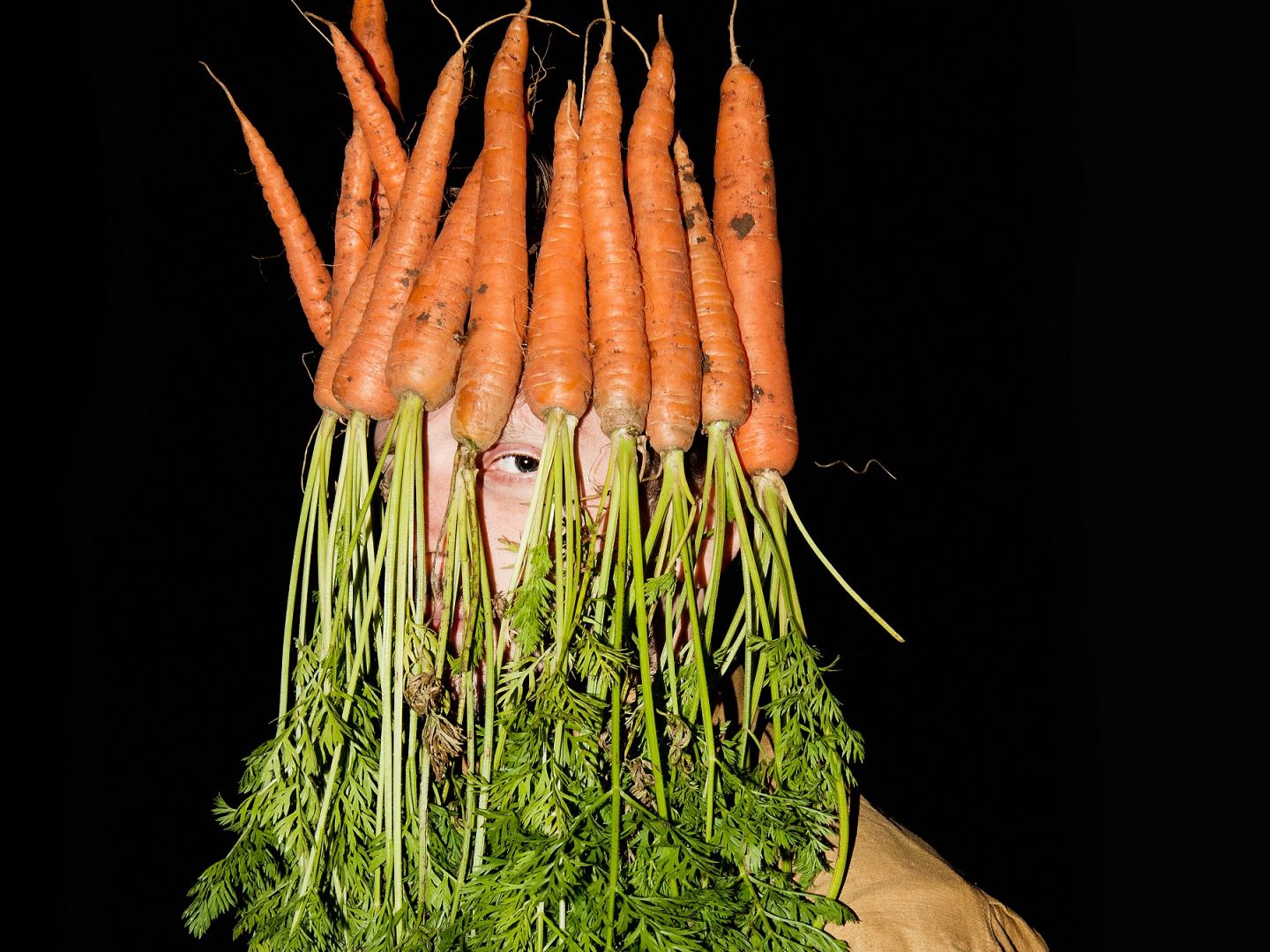 Plakatmotiv zu Über Menschen. Ein Mann trägt einen Strauß Möhren auf dem Kopf, die sein Gesicht verdecken.