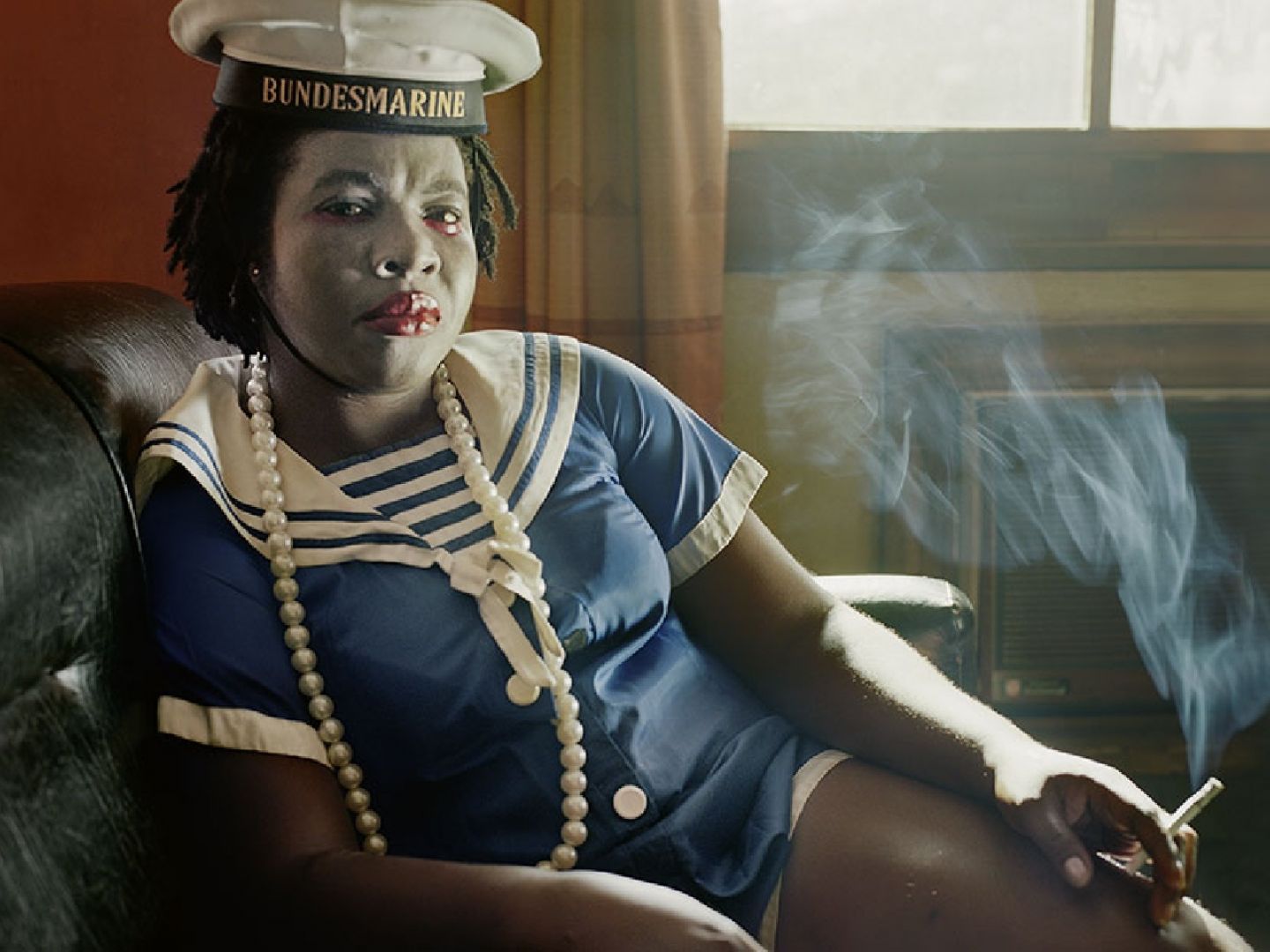 Plakatmotiv von Die Dreigroschenoper. Auf dem Bild sitzt eine Frau in Matrosen-Uniform mit rauchender Zigarette in der Hand.