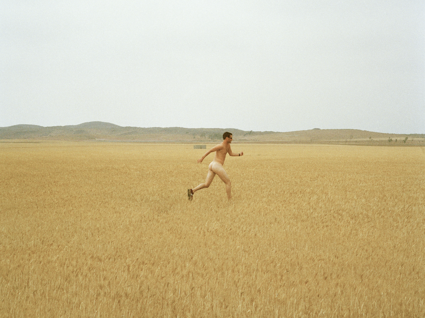 Das Foto zeigt einen nackten, laufenden Menschen auf einem Feld