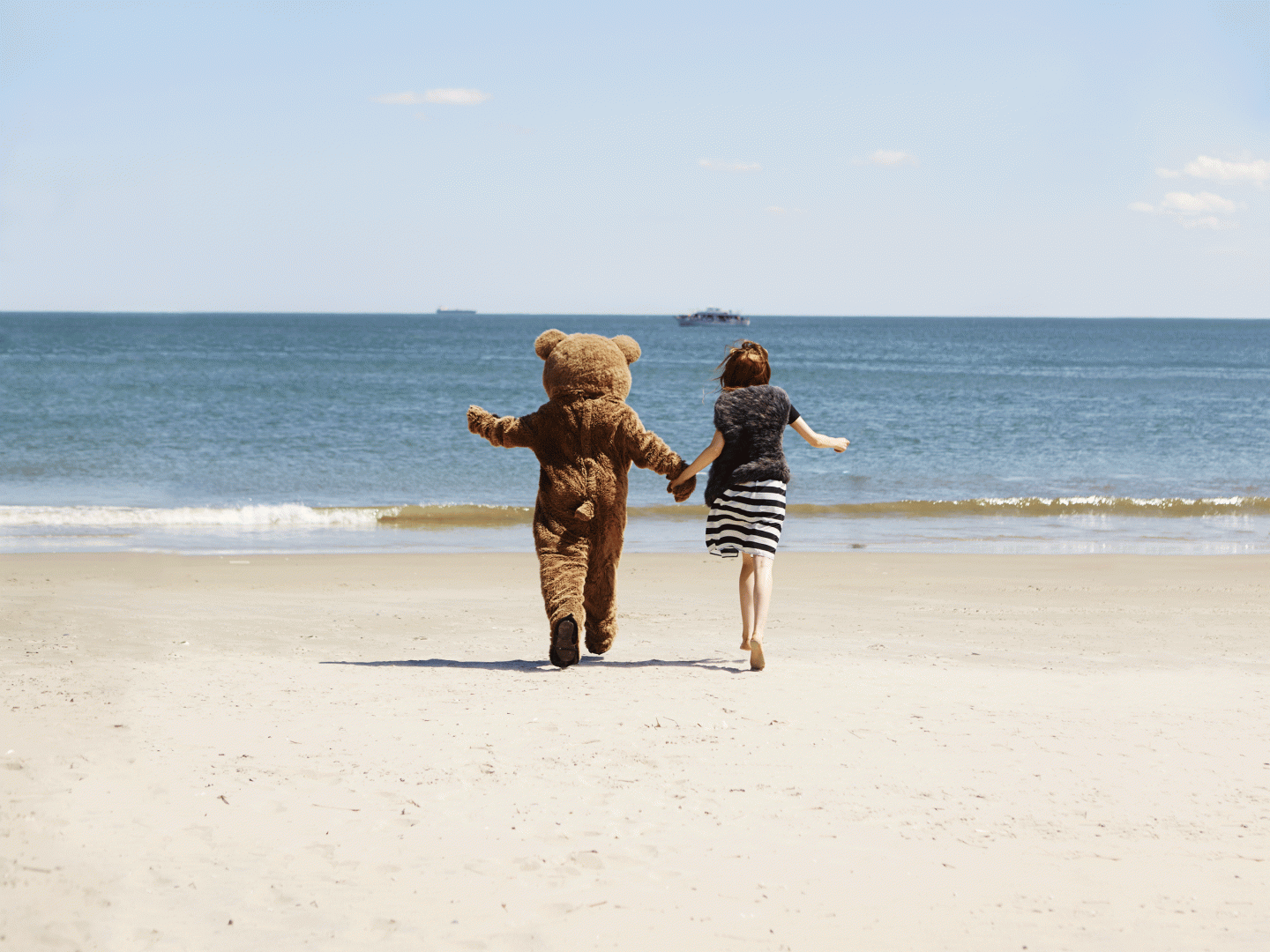 Ein Teddy und eine Frau spazieren am Strand