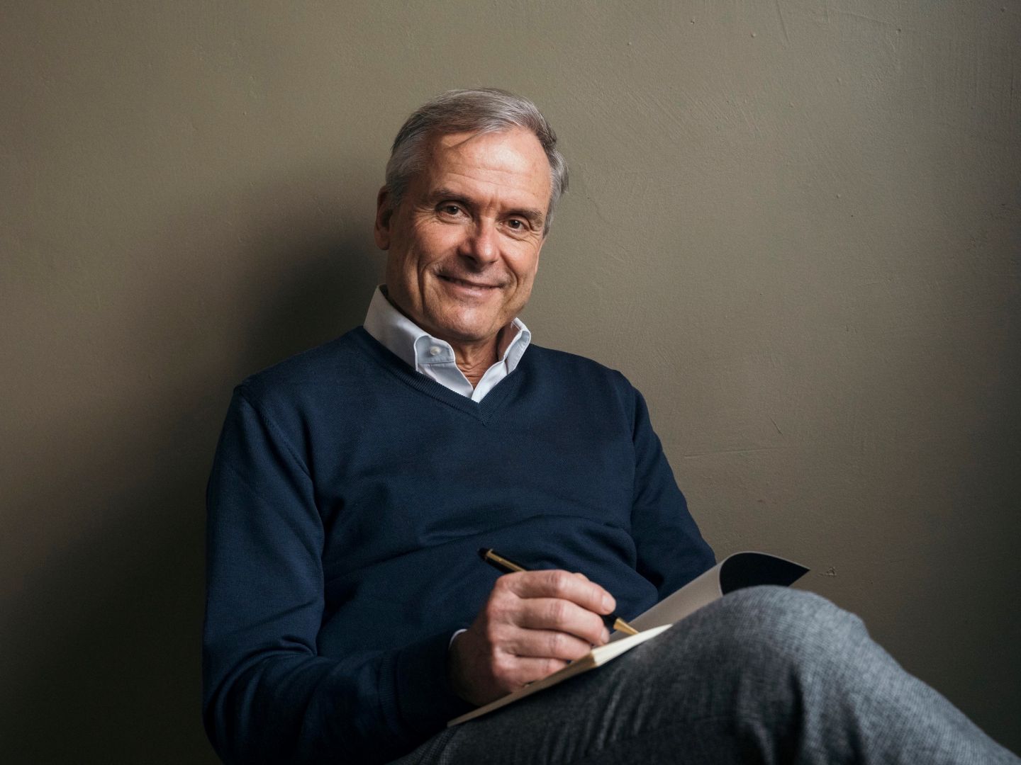 Ein Portraitfoto von Axel Hacke. Er sitzt und schreibt in ein Notizheft.