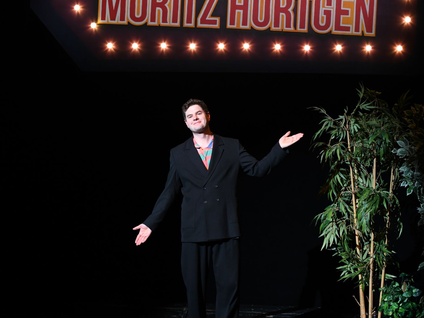 Moritz Hürtgen steht vor einem leuchtenden Schild mit dem der Aufschrift "Volksshow: Late Night mit Moritz Hürtgen""