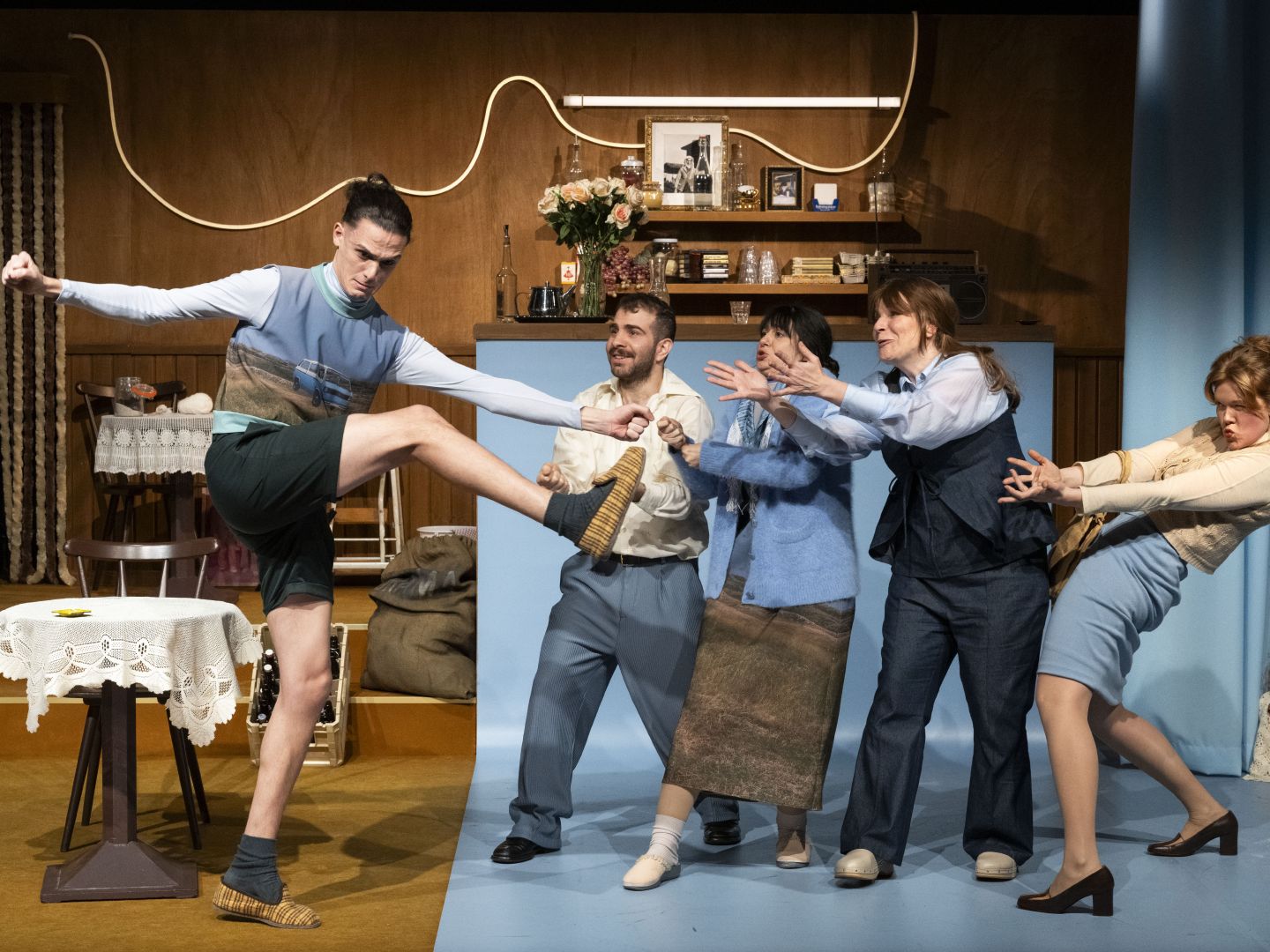 Fünf Schauspieler*innen stehen in einer Reihe. Die Person links außen kickt sein Bein in die Höhe.