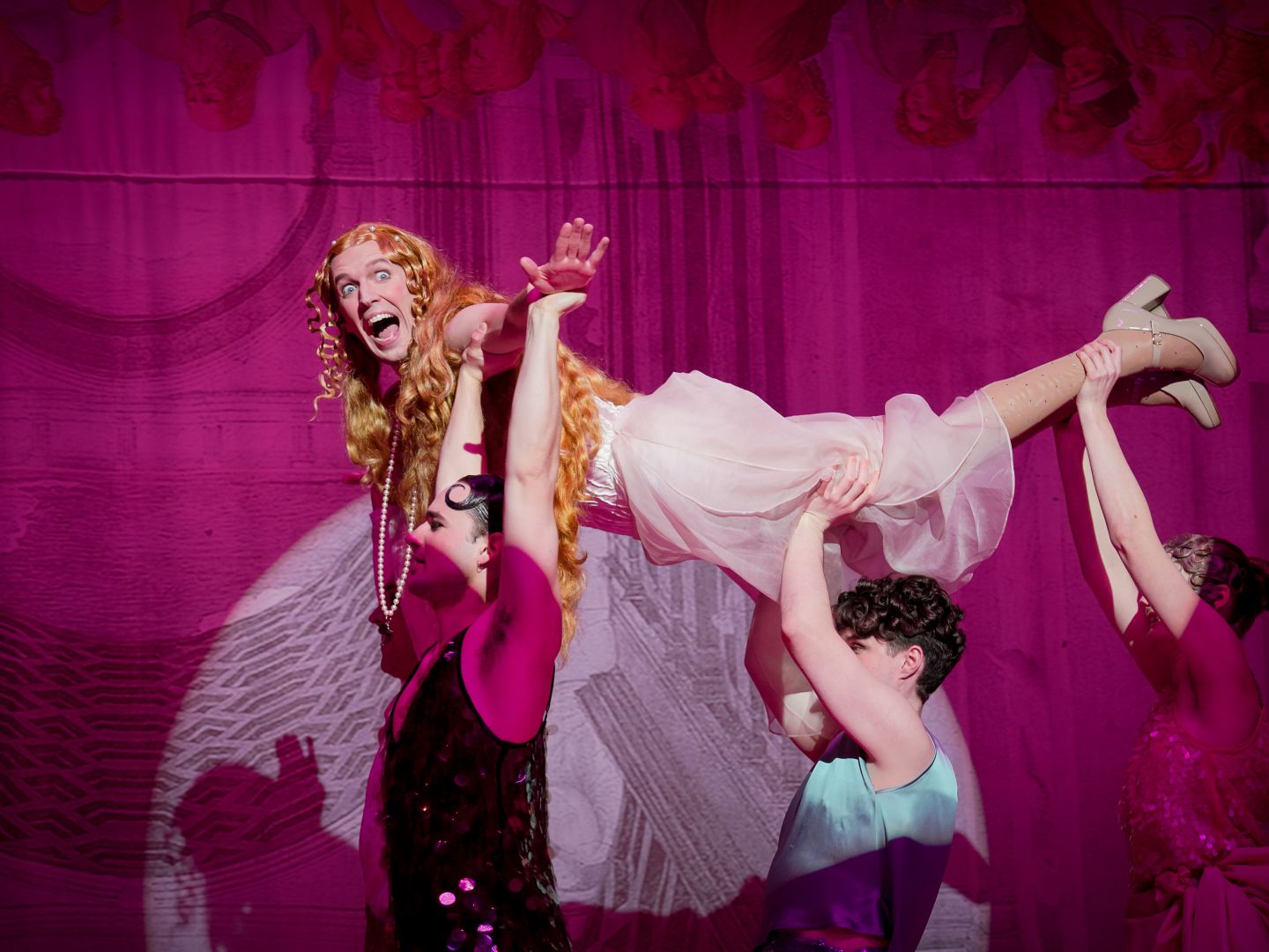 Caligula im Venuskostüm wird von drei anderen gehoben und &quot;fliegt&quot;.