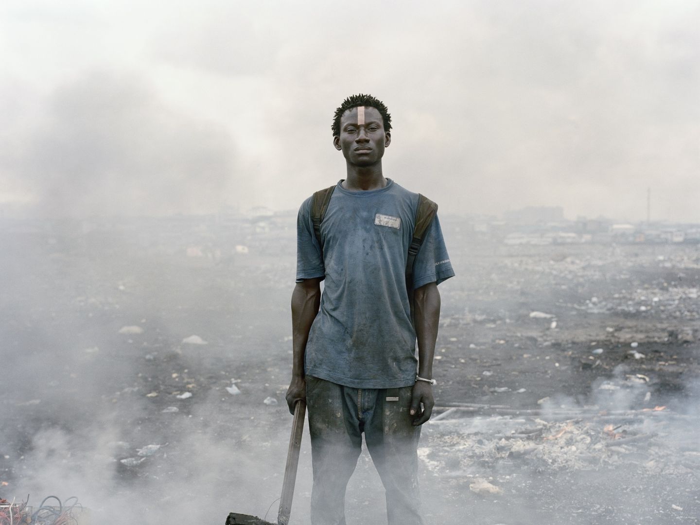 Ein junger Schwarzer Mann steht mit einer Hacke in der Hand inmitten von Schutt und Rauchwolken