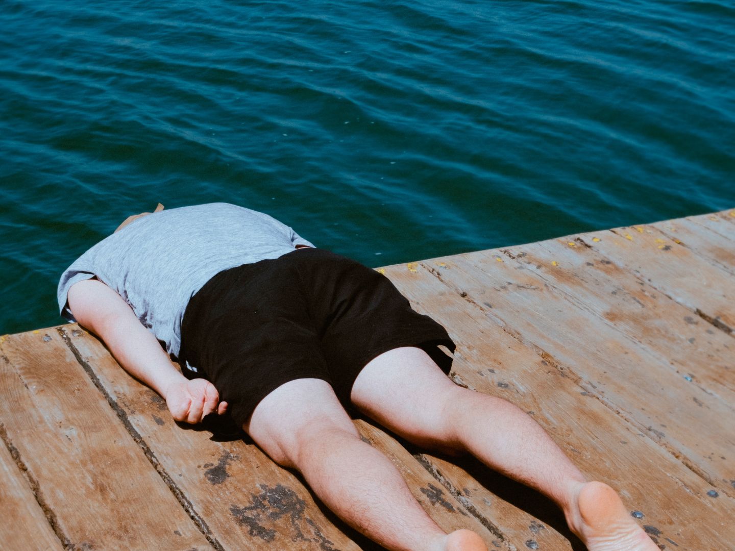 Das Plakatmotiv zeigt zeigt eine Person, die mit dem Bauch auf einem Steg liegt. Von den Schultern ab hängt der Körper über den Rand des Stegs hinaus, der Kopf ist nicht zu sehen.