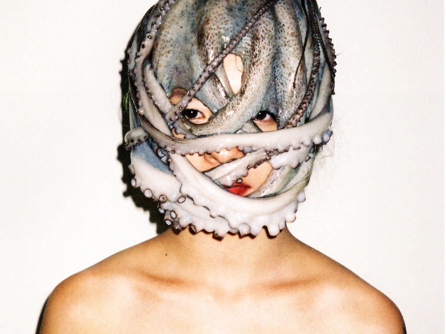 Eine Person vor weißem Hintergrund. Um ihren Kopf ist ein Oktopus gewickelt.