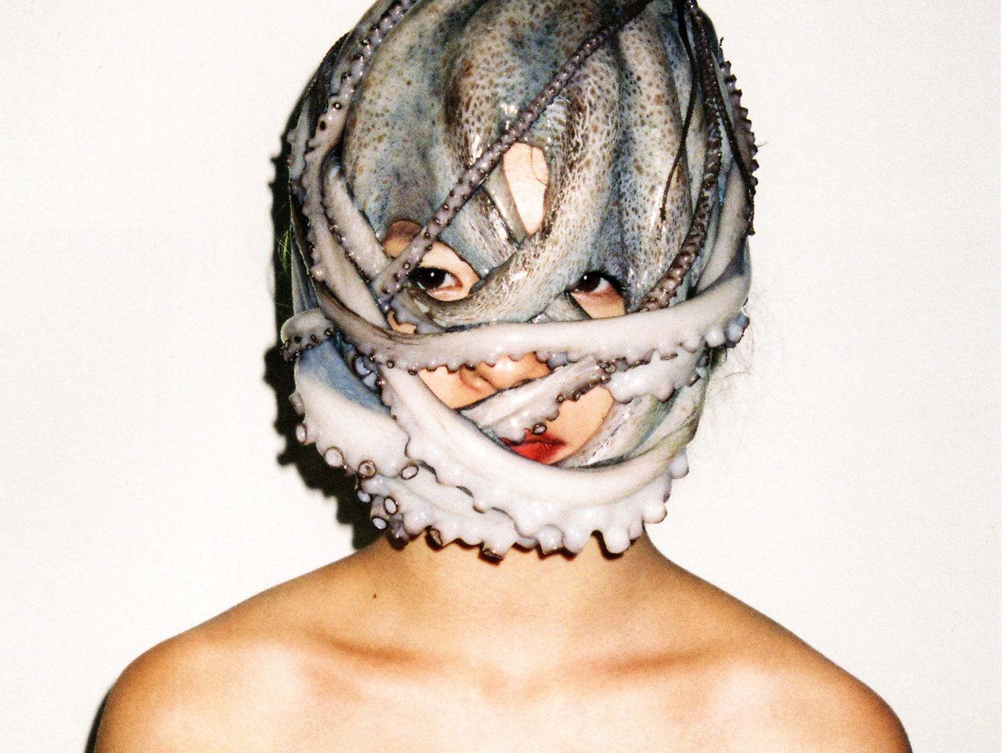 Eine Person vor weißem Hintergrund. Um ihren Kopf ist ein Oktopus gewickelt.