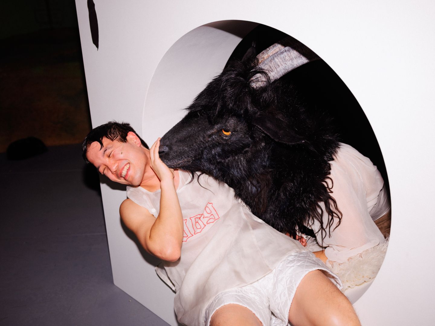 Kei Muramato liegt lächelnd an der Kante eines Tunneleingangs und drückt einen menschengroßen Ziegenkopf von sich weg