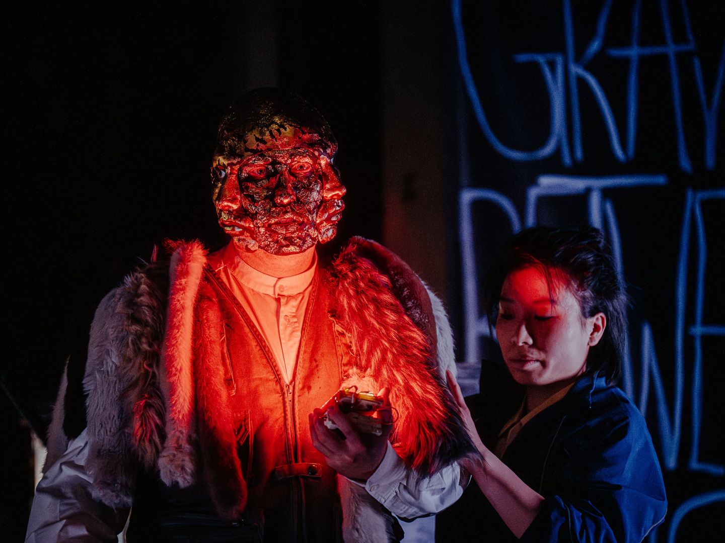 Ein maskierter Schauspieler leuchtet sich mit einem roten Licht an. Neben ihm eine Schauspielerin.