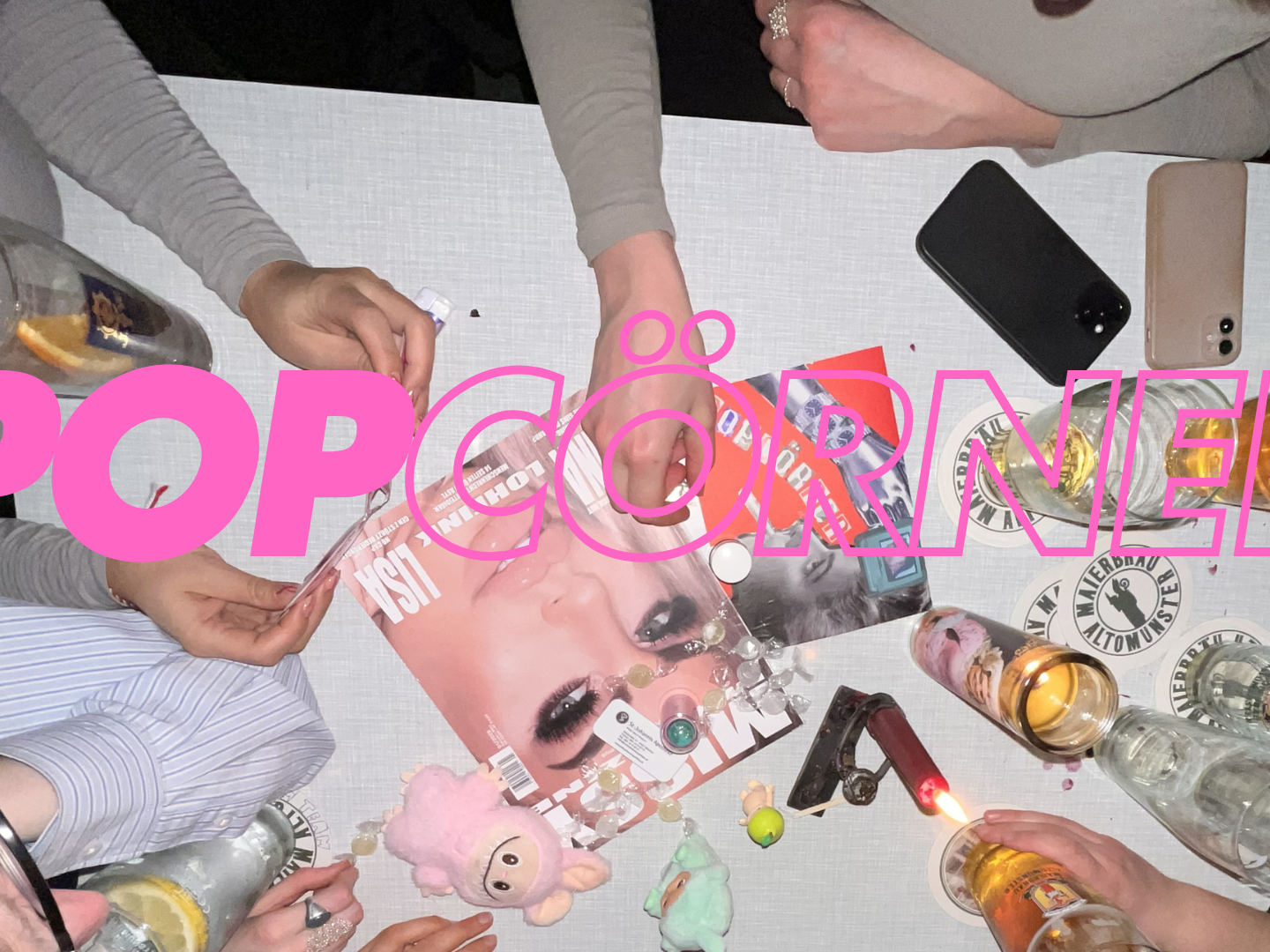 Ein Foto von einem Tisch voller Magazine und Gläser. Ringsherum sitzt eine Gruppe Frauen.