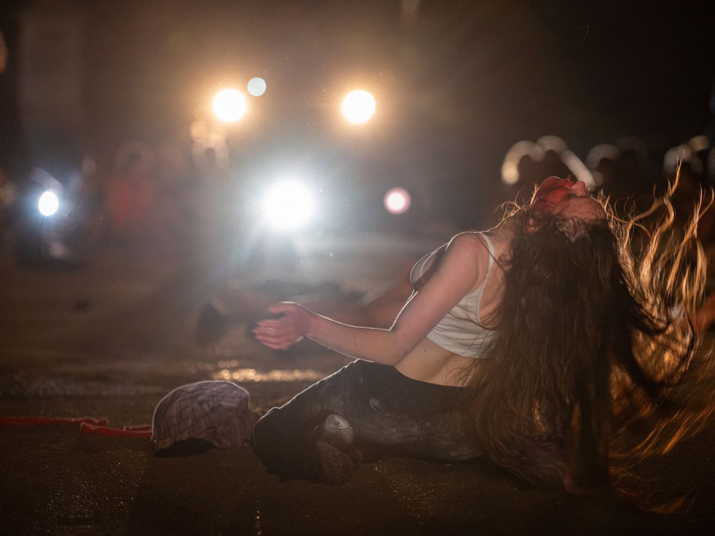Eine am Boden kniende Frau, deren Haare in Bewegung schwingen. Mehrere Lichtquellen strahlen wie Taschenlampen in Richtung Kamera.