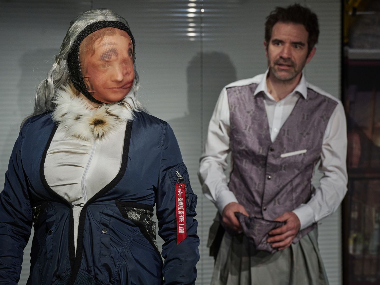 Eine Schauspielerin trägt eine Maske. Ein Schauspieler blickt sie unsicher an.