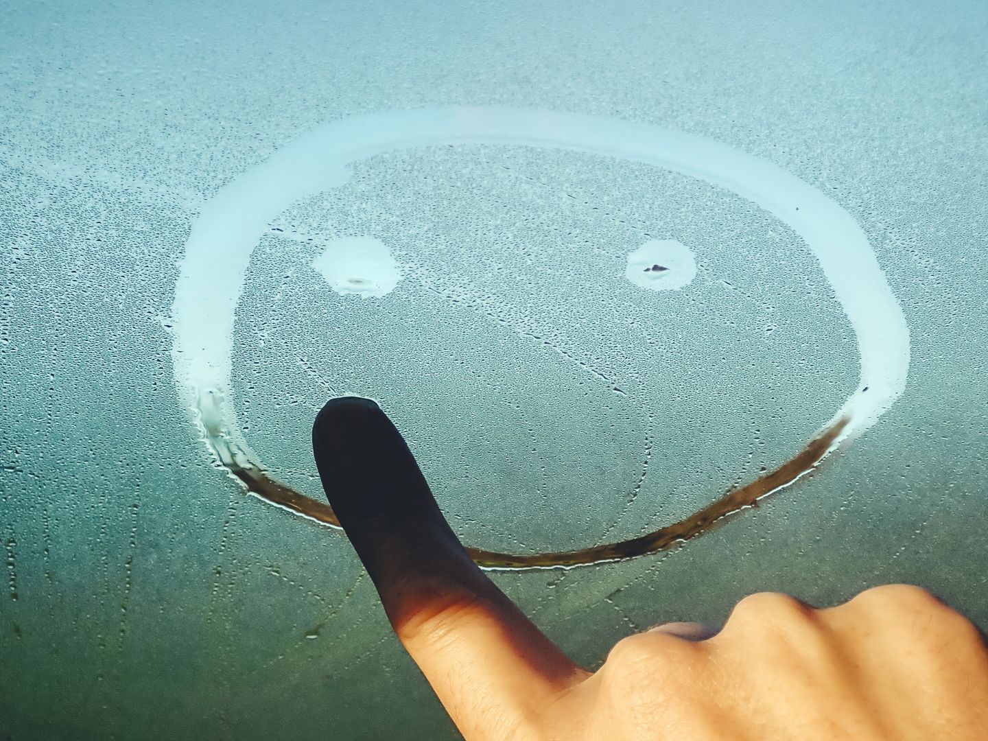 Eine Hand malt einen Smiley auf ein beschlagenes Glas.
