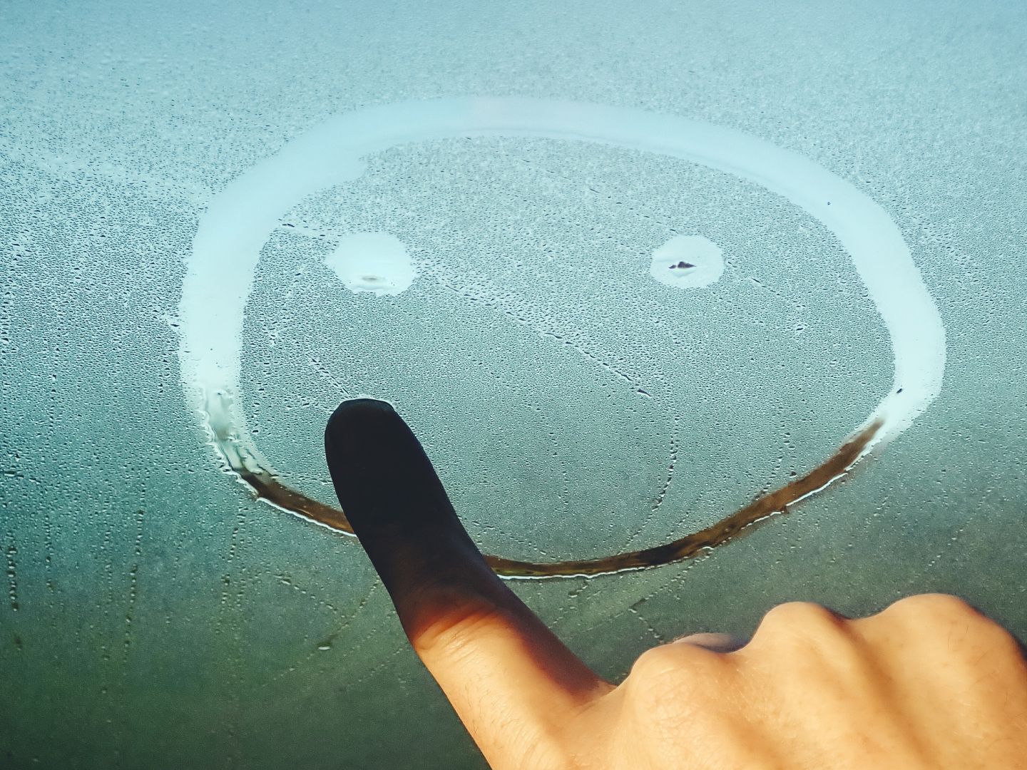 Eine Hand malt einen Smiley auf ein beschlagenes Glas.