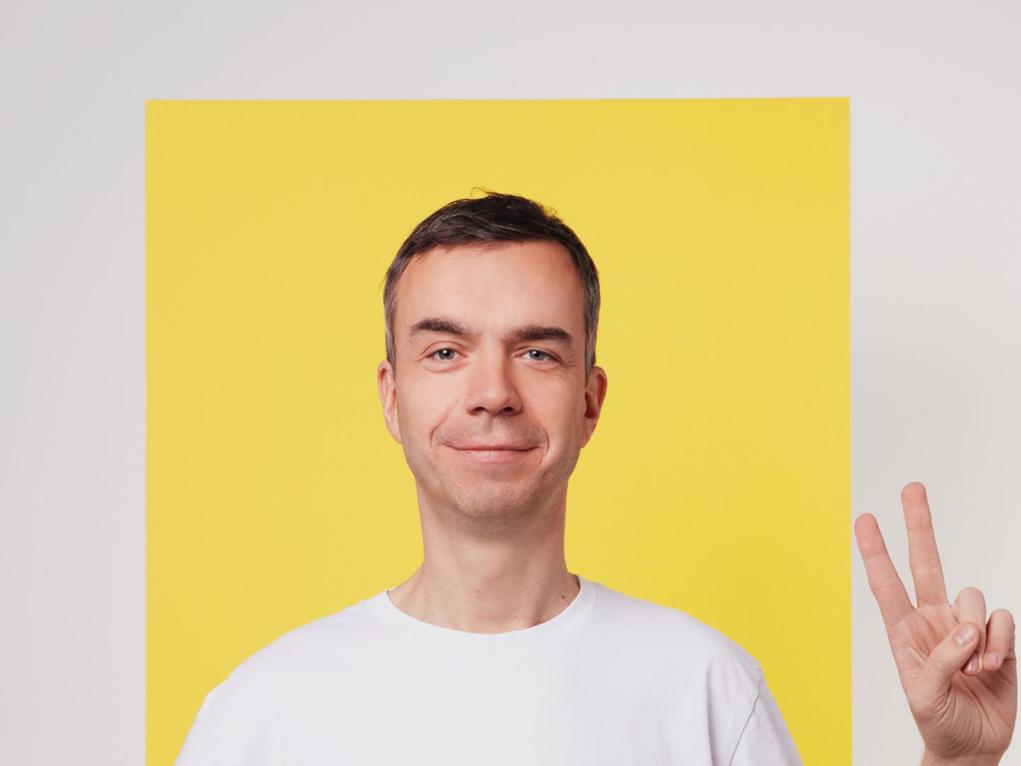 Foto von Matze Hielscher, der mit seiner Hand das Peace-Zeichen macht, vor gelbem Hintergrund.