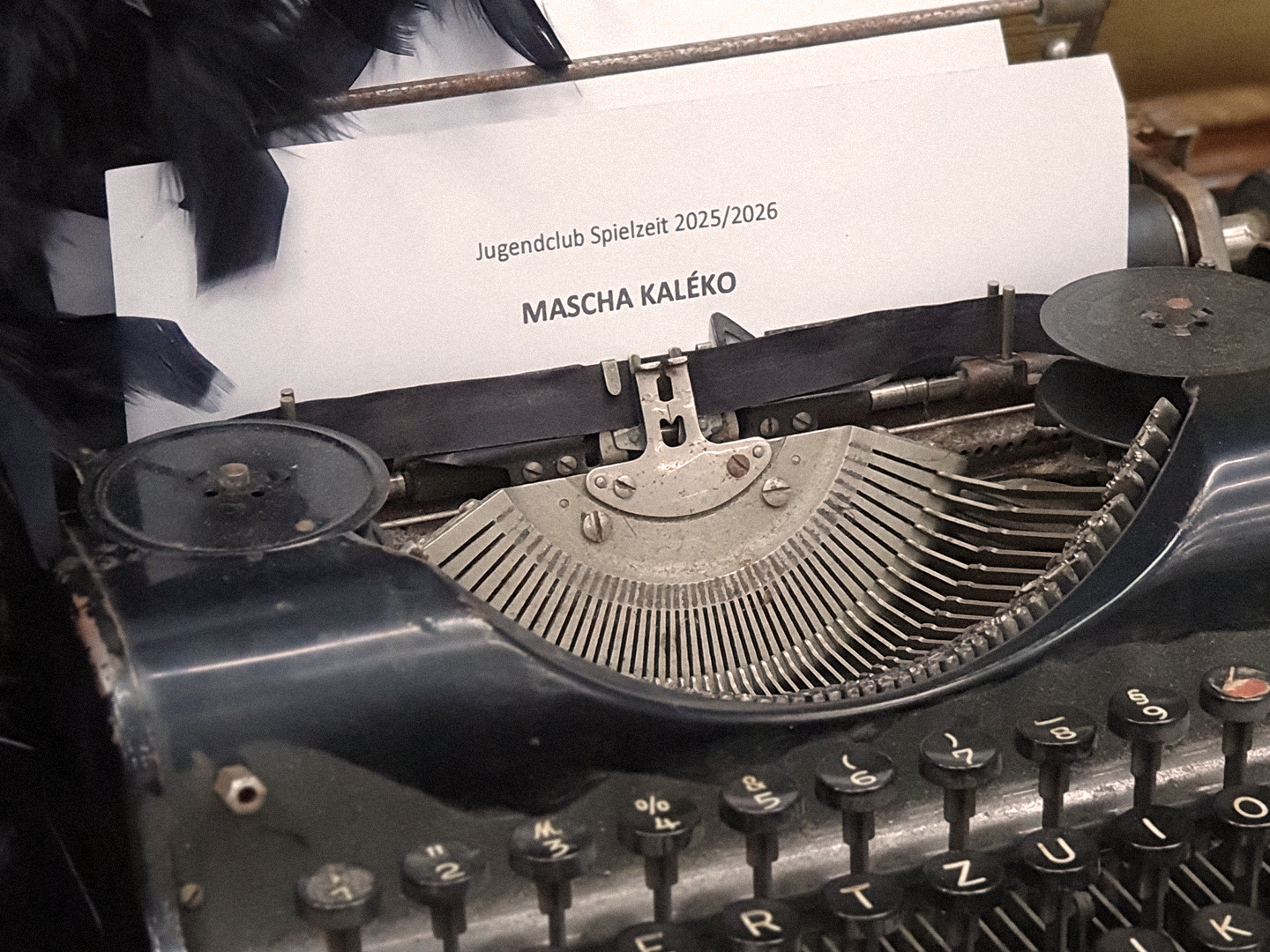 Eine Schreibmaschine aus der ein Blatt ragt. Darüber ist eine schwarze Federboa drapiert.