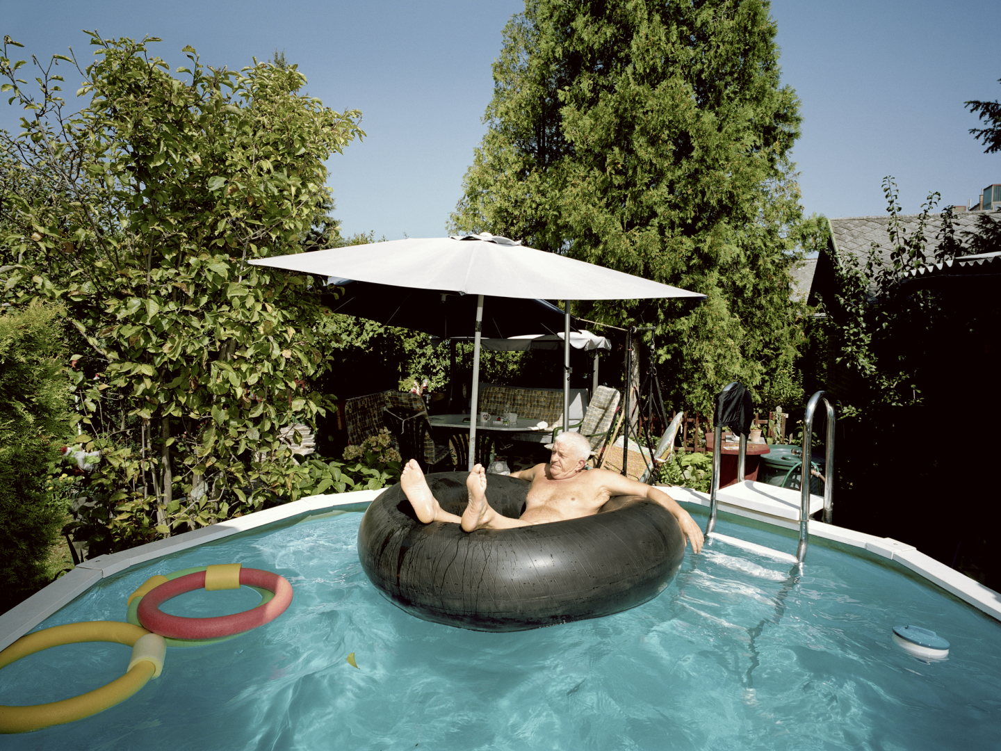 Ein alter Mann sitzt in einem Schwimmring in einem Gartenpool.