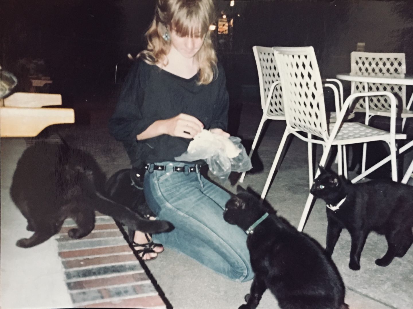 Das Bild zeigt ein Foto von Jessica Rockstroh mit vier schwarzen Katzen, welche sie auf einer Terrasse füttert.