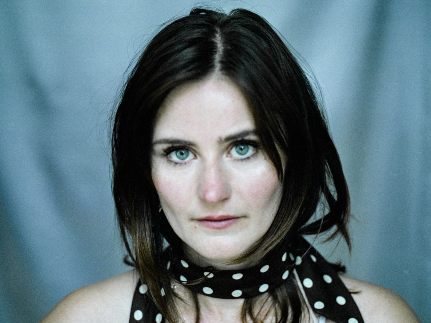 Ein Portraitfoto von Eleonore Carrière vor blauem Hintergrund mit einem gepunkteten Halztuch.