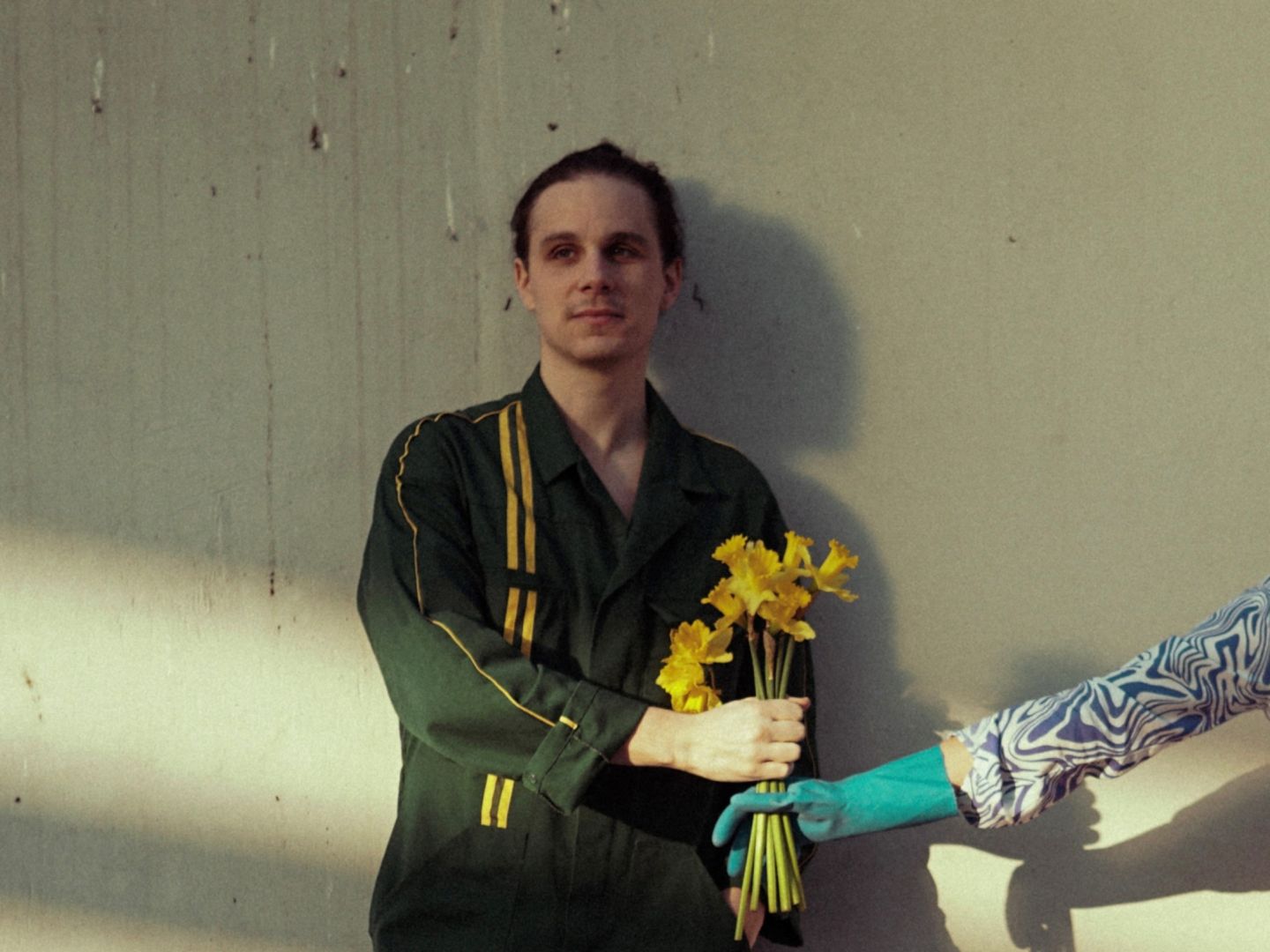 Alexander Zwick steht vor einer Wand und ihm wird ein gelber Blumenstrauß in die Hand gereicht.