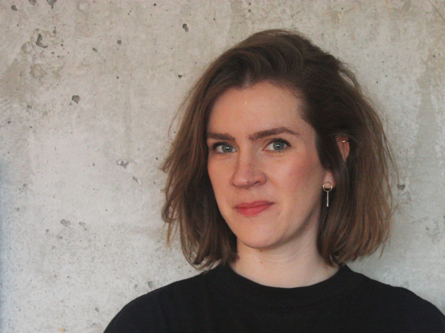 Nadin Schumacher steht vor einer Wand und trägt ein  schwarzes T-Shirt.